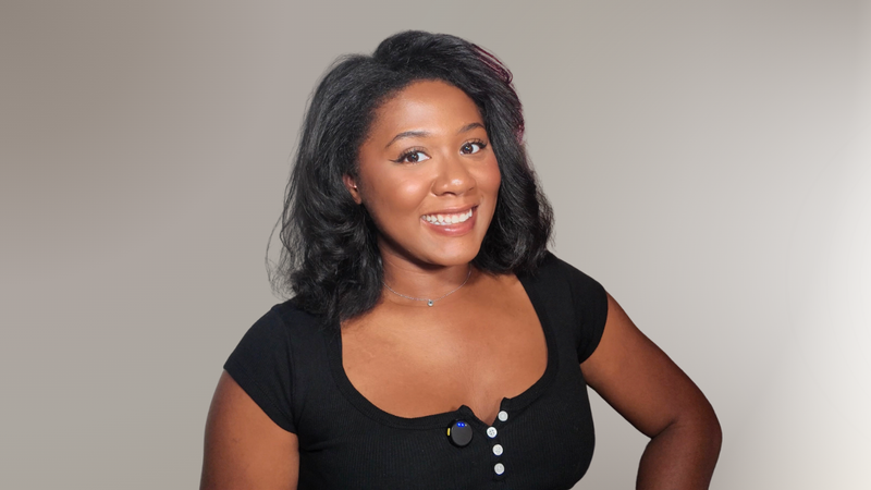 Kayla Sharee wearing a black top with buttons on a plain background